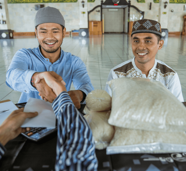 Dos hombres musulmanes dándose la mano mientras uno recibe arroz y dinero como Zakat