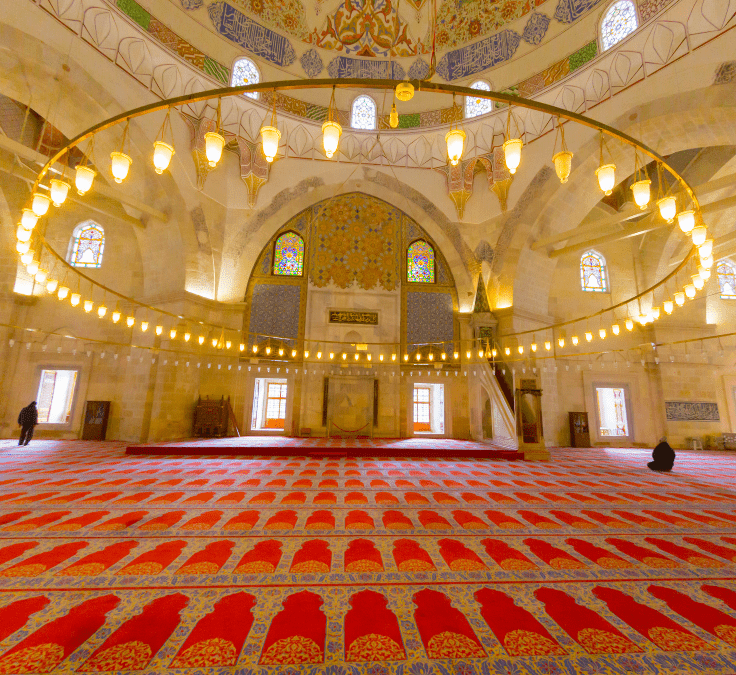 Interior de una mezquita con gran lámpara y alfombra roja representando unidad espiritual