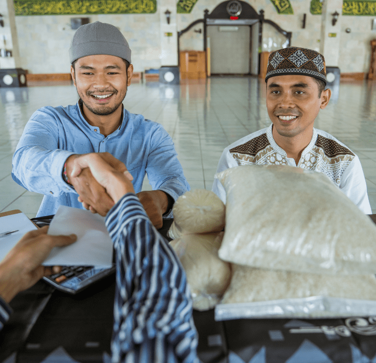 Dos hombres musulmanes dándose la mano mientras uno recibe arroz y dinero como Zakat